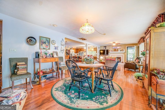 dining area with light wood finished floors, a tiled fireplace, and a ceiling fan