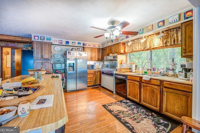 kitchen with a textured ceiling, stainless steel appliances, a sink, light wood-style floors, and brown cabinets