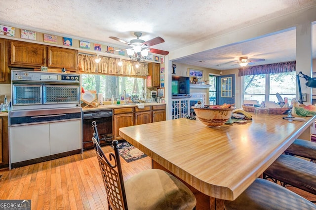 dining space with a textured ceiling, ceiling fan, a fireplace, and light wood-style floors