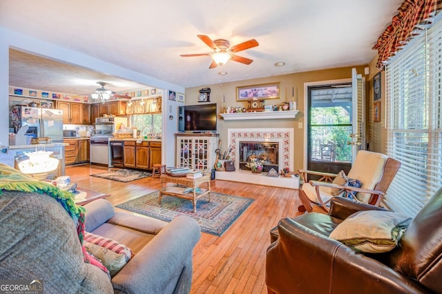 living room with ceiling fan, light wood-style flooring, and a tiled fireplace