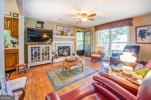 living room with ceiling fan, a glass covered fireplace, and wood finished floors