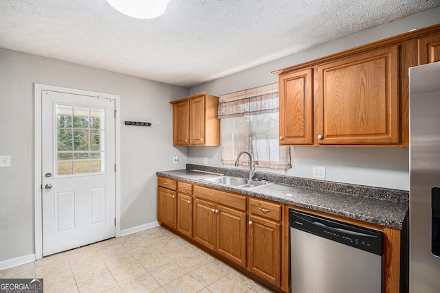 kitchen with dark countertops, appliances with stainless steel finishes, brown cabinetry, and a sink