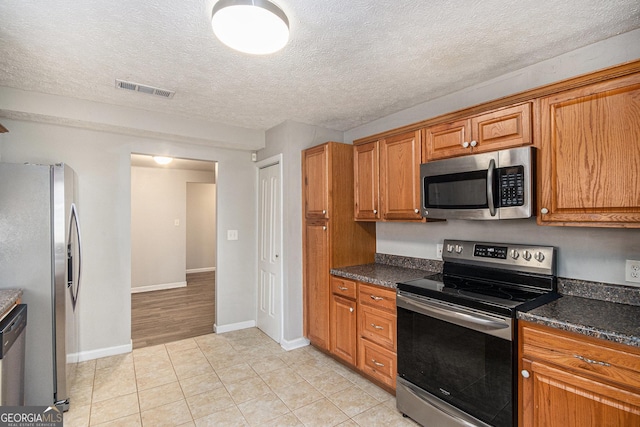 kitchen with dark countertops, visible vents, appliances with stainless steel finishes, and brown cabinets