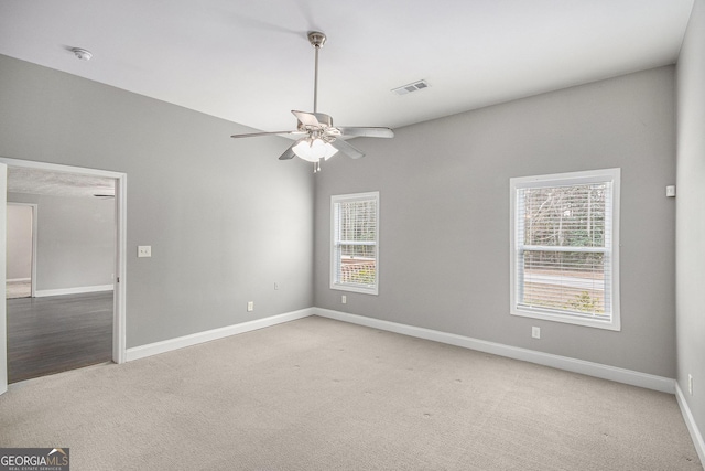 spare room featuring light colored carpet, ceiling fan, visible vents, and baseboards