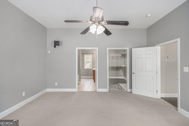 unfurnished bedroom with a walk in closet, a closet, carpet flooring, and baseboards