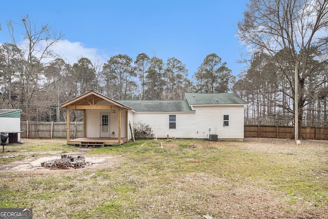 rear view of house featuring a fire pit, a fenced backyard, cooling unit, and a lawn