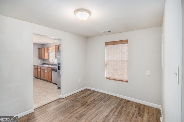 empty room with light wood-type flooring, visible vents, a sink, and baseboards