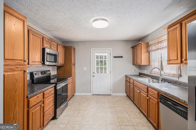 kitchen with stainless steel appliances, dark countertops, brown cabinetry, and a sink