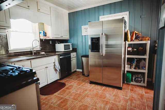 kitchen featuring crown molding, light tile patterned floors, dark countertops, appliances with stainless steel finishes, and a sink