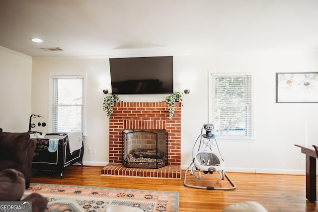 living room featuring a fireplace, visible vents, ornamental molding, wood finished floors, and baseboards