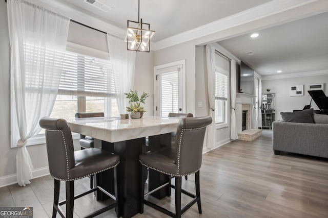 dining space with visible vents, a fireplace with raised hearth, wood finished floors, and ornamental molding