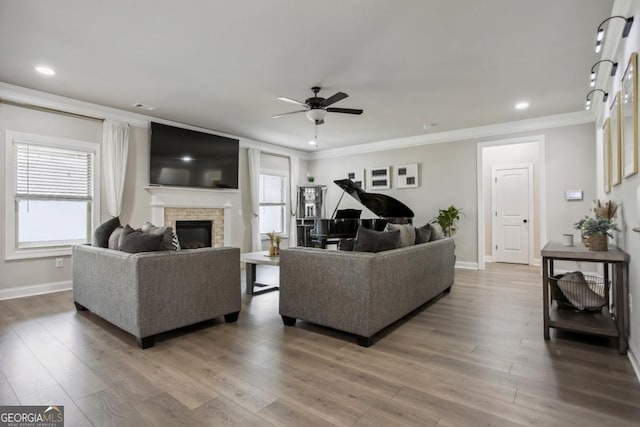 living area featuring a ceiling fan, baseboards, light wood-style floors, ornamental molding, and a glass covered fireplace