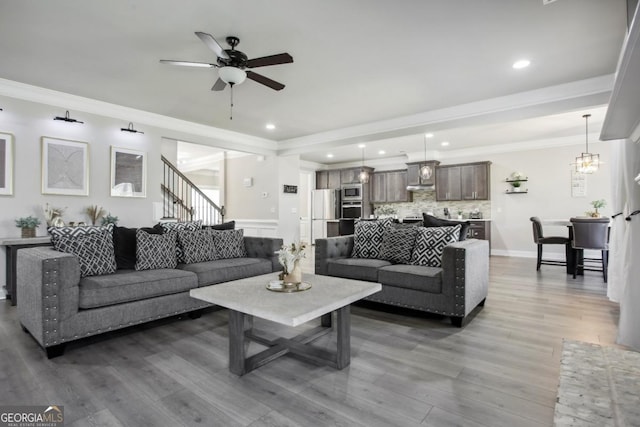 living area with stairway, ornamental molding, wood finished floors, and ceiling fan with notable chandelier