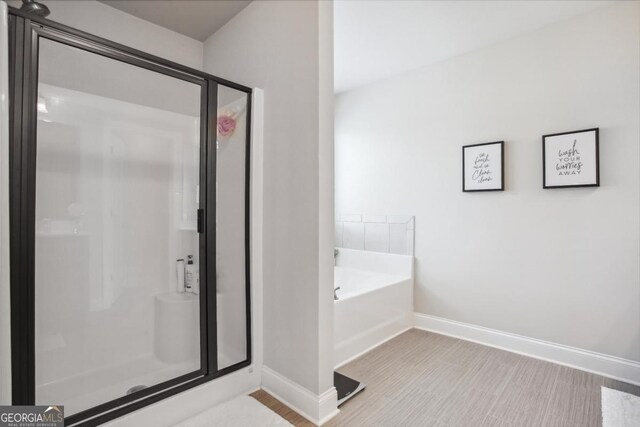 bathroom with a shower stall, baseboards, a bath, and wood finished floors