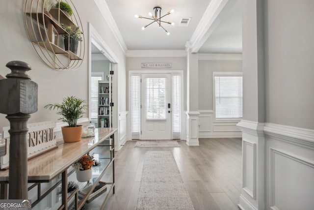 entryway with ornamental molding, a chandelier, visible vents, and wood finished floors