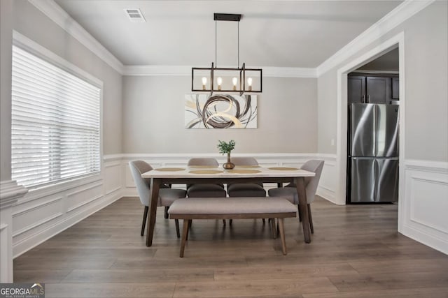 dining area with visible vents, ornamental molding, dark wood-style flooring, a chandelier, and a decorative wall