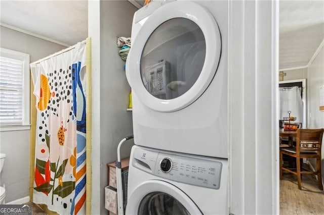 laundry area featuring stacked washer and dryer, wood finished floors, laundry area, and crown molding