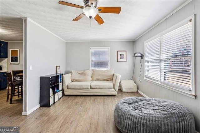 living area featuring ceiling fan, baseboards, wood finished floors, and crown molding