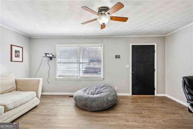 living area with crown molding, ceiling fan, wood finished floors, and baseboards