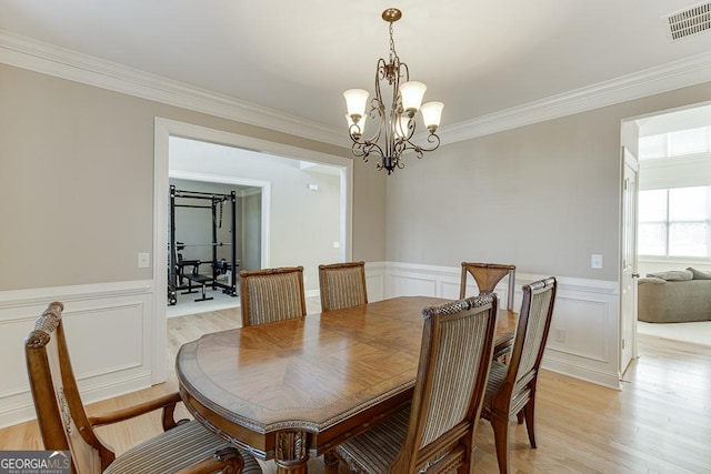 dining area featuring a wainscoted wall, a notable chandelier, visible vents, light wood-style floors, and ornamental molding