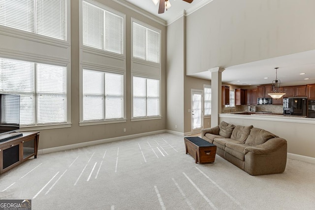 living area featuring light carpet, crown molding, a towering ceiling, and ornate columns