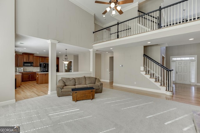 living area with decorative columns, stairway, a towering ceiling, ornamental molding, and baseboards