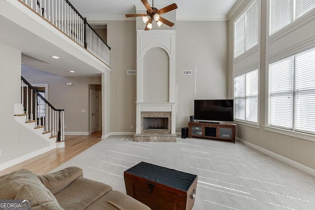 living area featuring baseboards, a ceiling fan, stairway, ornamental molding, and a high ceiling