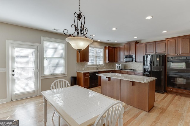 kitchen with a center island, light wood finished floors, tasteful backsplash, a sink, and black appliances