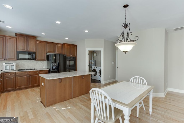 kitchen featuring light wood finished floors, visible vents, washing machine and dryer, a kitchen island, and black appliances