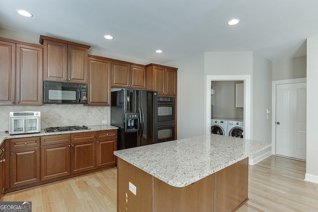 kitchen featuring light wood finished floors, black appliances, separate washer and dryer, and light stone countertops