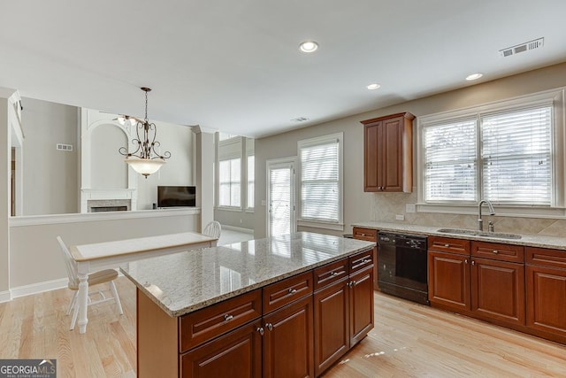 kitchen with black dishwasher, light wood finished floors, a fireplace, and a sink