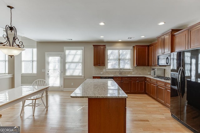 kitchen featuring decorative backsplash, light wood-style flooring, a kitchen island, light stone countertops, and black appliances