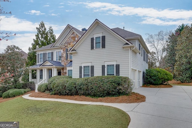 view of front of house featuring a garage, driveway, stone siding, a standing seam roof, and a front yard