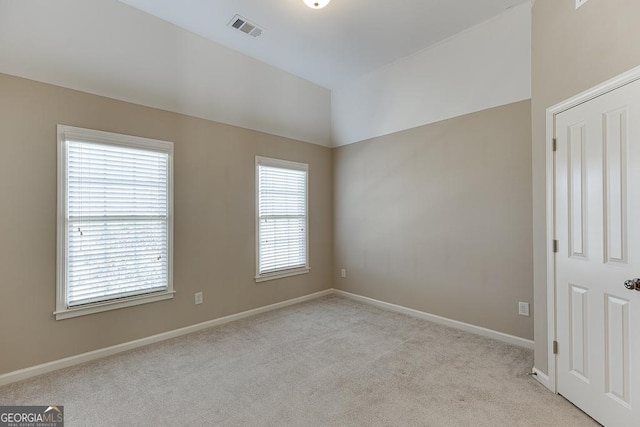 empty room with visible vents, vaulted ceiling, light carpet, and baseboards