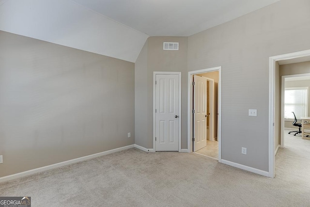 unfurnished bedroom featuring light carpet, baseboards, visible vents, and lofted ceiling