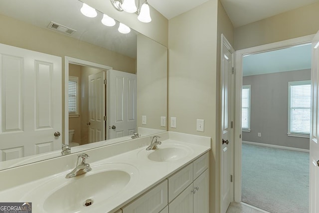 bathroom with visible vents, a sink, toilet, and double vanity