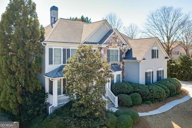 view of front of home with stone siding, a shingled roof, and a chimney