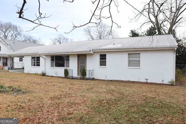 rear view of house with concrete block siding, metal roof, and a lawn