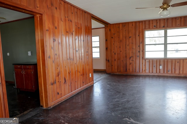 empty room with a ceiling fan, crown molding, wood walls, and baseboards