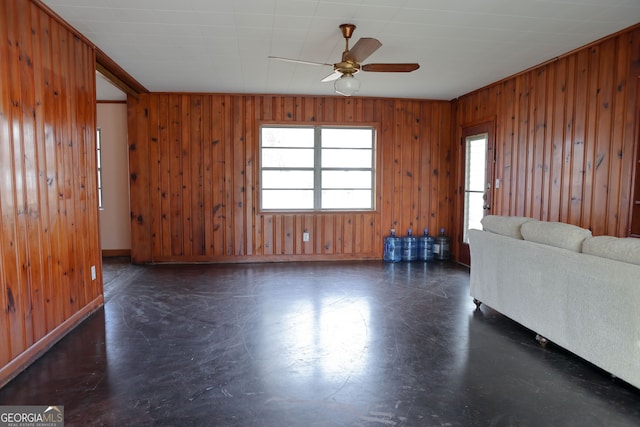 unfurnished living room with ceiling fan and wood walls