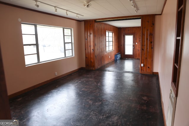 unfurnished room featuring concrete flooring, wood walls, baseboards, ornamental molding, and track lighting