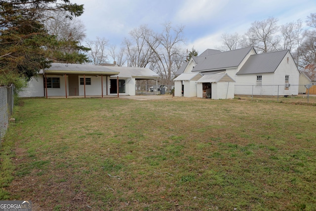 back of property with a fenced backyard, metal roof, an attached carport, an outbuilding, and a yard