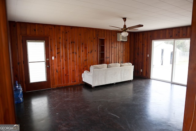 unfurnished living room with a ceiling fan, wooden walls, and a wall mounted AC