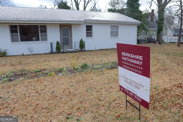 ranch-style house with concrete block siding, metal roof, and a front yard