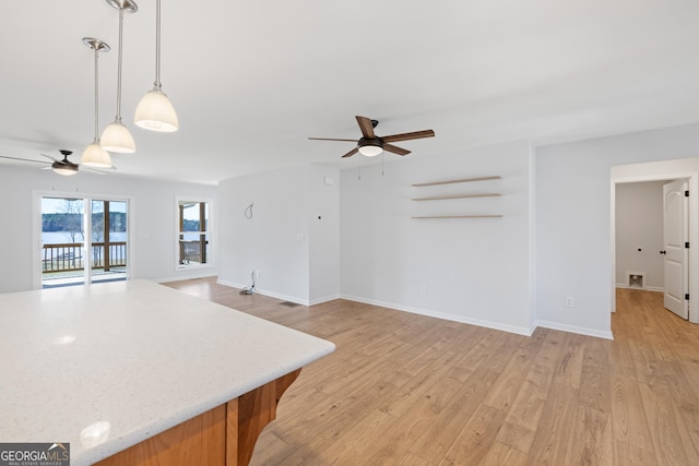 kitchen with a ceiling fan, open floor plan, hanging light fixtures, light stone countertops, and light wood finished floors