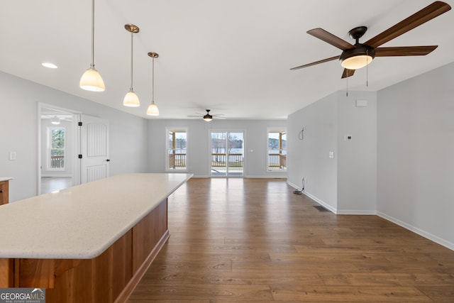 kitchen with ceiling fan, dark wood-style flooring, a kitchen island, baseboards, and pendant lighting