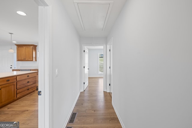 corridor featuring attic access, visible vents, light wood-style floors, and baseboards