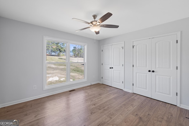 unfurnished bedroom with two closets, visible vents, a ceiling fan, wood finished floors, and baseboards