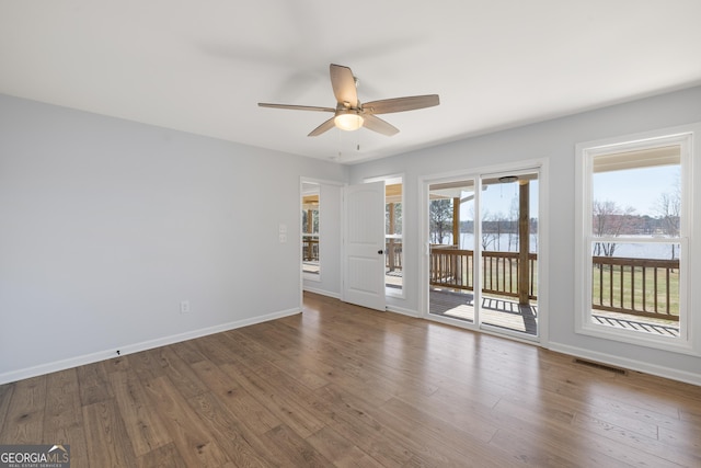 spare room with a water view, wood finished floors, a ceiling fan, visible vents, and baseboards