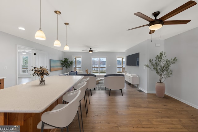 interior space featuring baseboards, open floor plan, wood finished floors, a kitchen breakfast bar, and pendant lighting